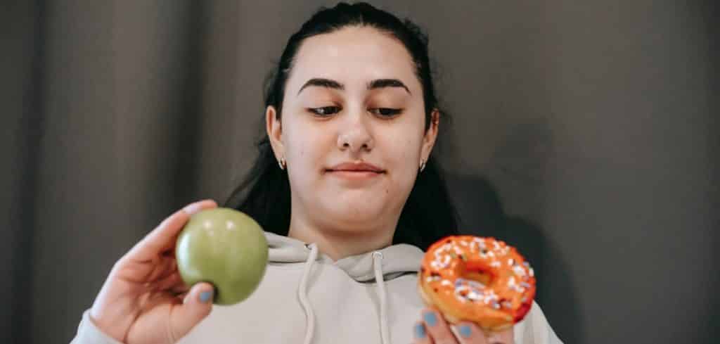 características de la toma de decisiones, mujer eligiendo si comerse una dona o una manzana